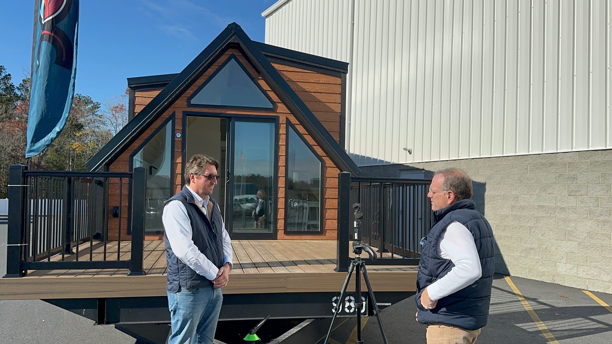 Two men talking on the porch of an A-frame cottage outside the factory