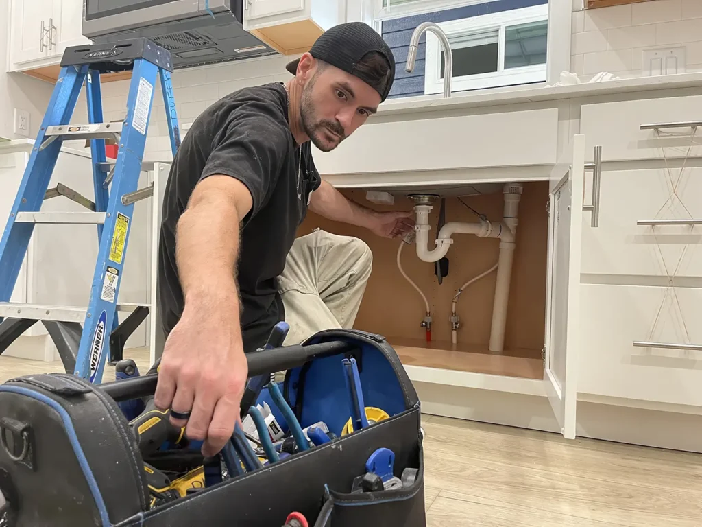 Technician repairing plumbing under a cottage sink